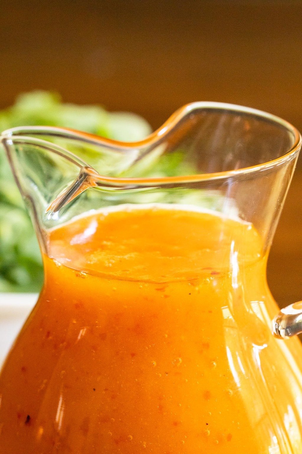Vertical closeup photo of a glass pitcher of Red Pepper Jelly Salad Dressing.
