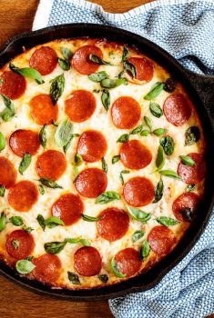 Horizontal overhead photo of an Easy Deep Dish Pepperoni Pizza in a black skillet on a wood table.