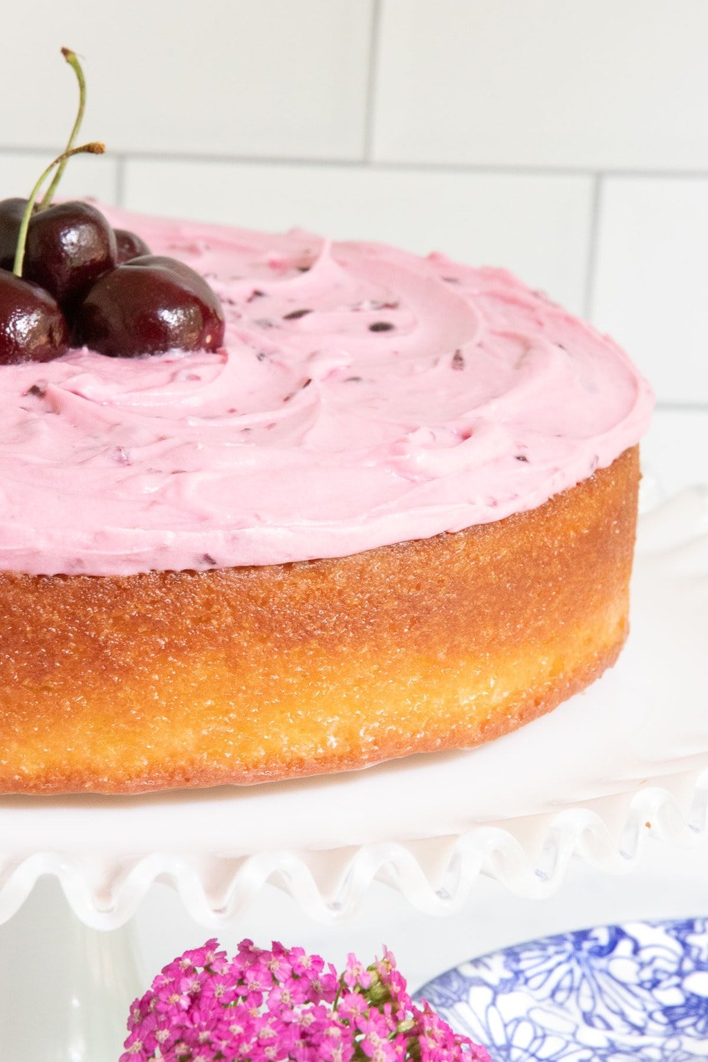 Vertical closeup photo of a Easy French Almond Cake with Fresh Cherry Buttercream on a white glass pedestal cake stand.