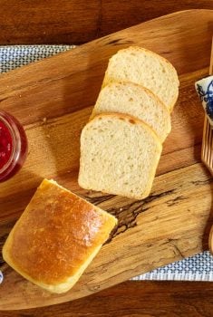Horizontal overhead photo of Every Day Easy Brioche Bread on a wood cutting board with a slab of butter and a jar of raspberry jam.