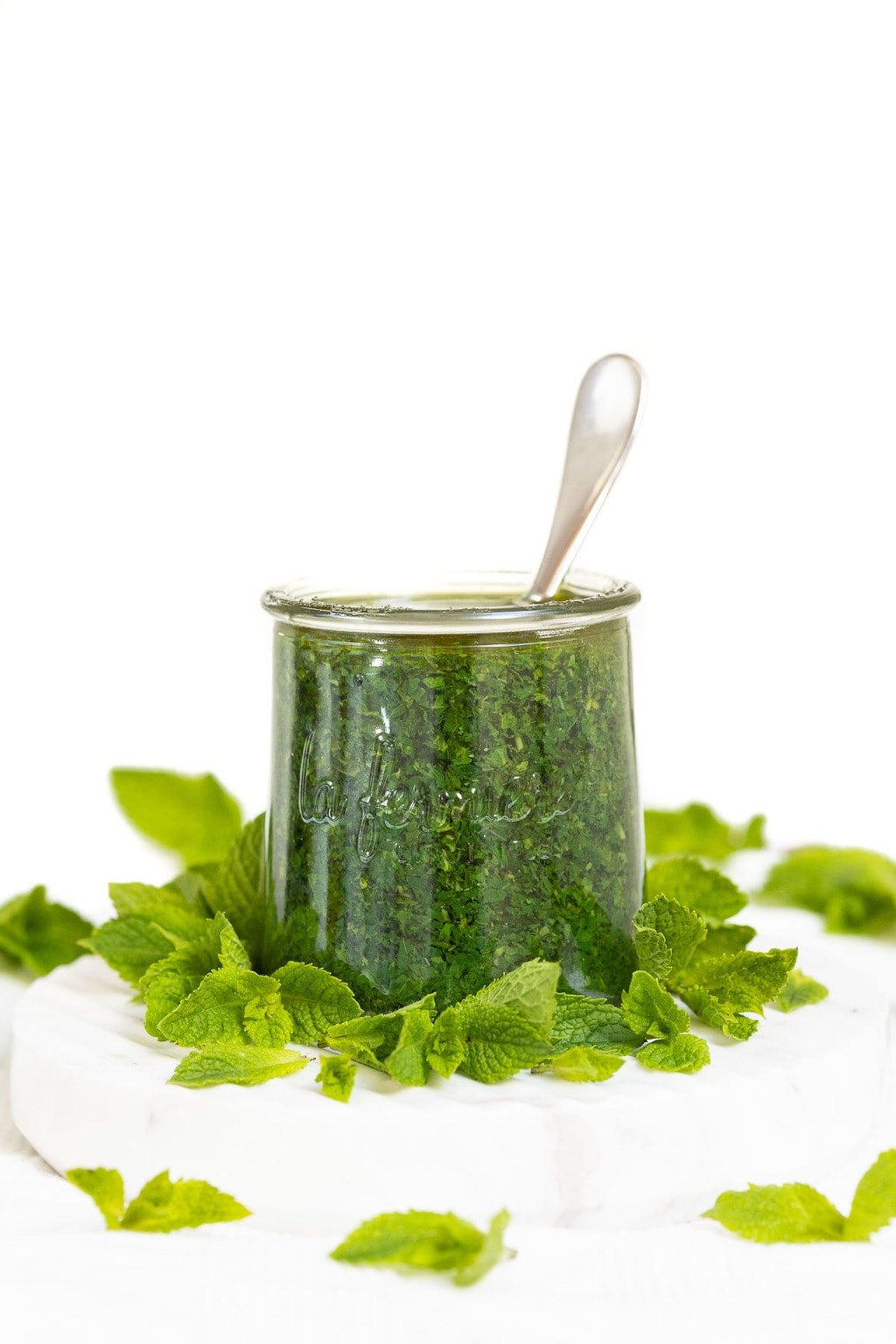 Vertical closeup photo of Italian Mint Pesto in a Weck glass jar surrounded by fresh mint leaves.