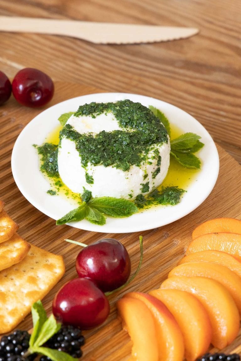 Mint Pesto on cheese on a white plate with fresh fruit.