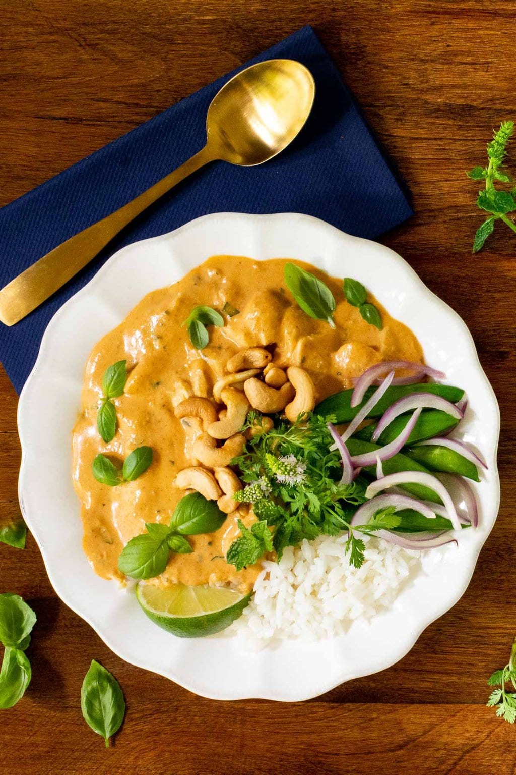 Vertical overhead photo of a bowl of 30-Minute Basil Coconut Chicken with sides of rice and fresh snow peas and garnished with lime wedges and fresh basil leaves.
