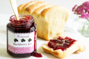 blackberry freezer jam spread on a piece of homemade toast with a custom labeled jar sitting beside the loaf