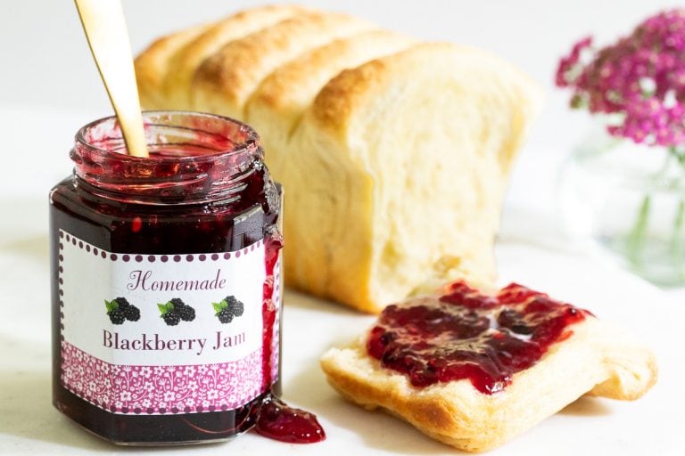 blackberry freezer jam spread on a piece of homemade toast with a custom labeled jar sitting beside the loaf