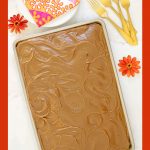 Vertical photo of a Ridiculously Easy Caramel Buttermilk Sheet Cake on a white marble surface. The photo has an orange border and the cake is surrounded by orange zinnias.