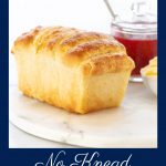Vertical photo of a loaf of No Knead Pull-Apart Bread on a round marble surface with a glass jar of raspberry freezer jam and a dish of fresh butter in the background.