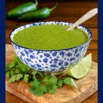 Vertical closeup photo of a serving bowl of Mexican Cilantro Sauce - thecafesucrefarine.com surrounded by fresh cilantro leaves and lime wedges.