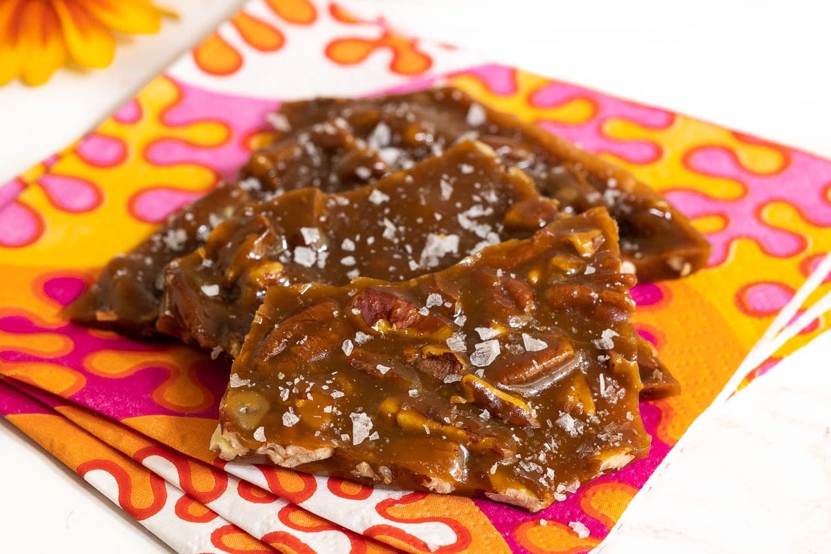Horizontal closeup photo of pieces of Sea Salted Pumpkin Pecan Brittle on a colorful orange, pink and yellow napkin.