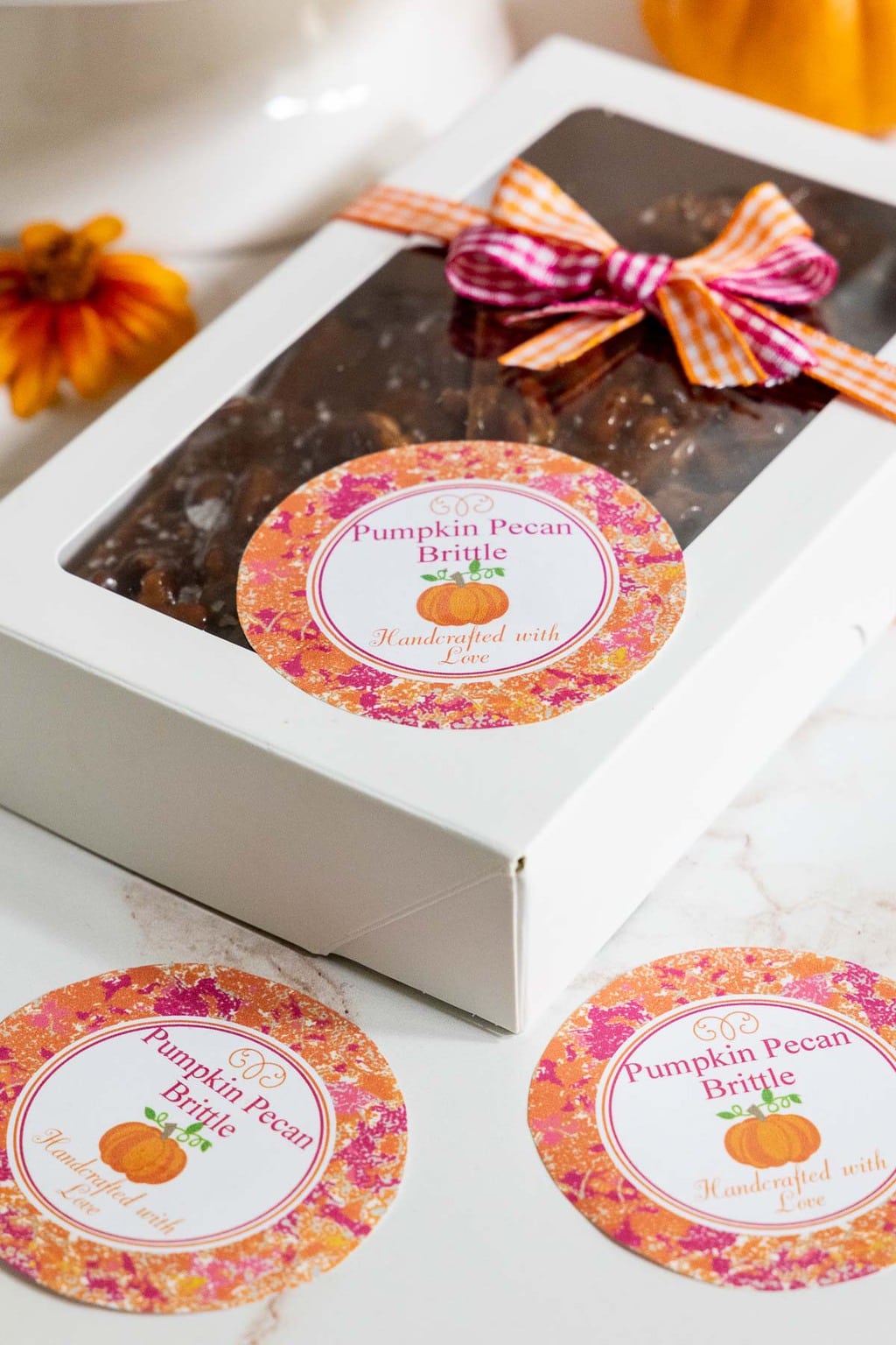Vertical photo of a gift box filled with Sea Salted Pumpkin Pecan Brittle with custom gift labels on the box.