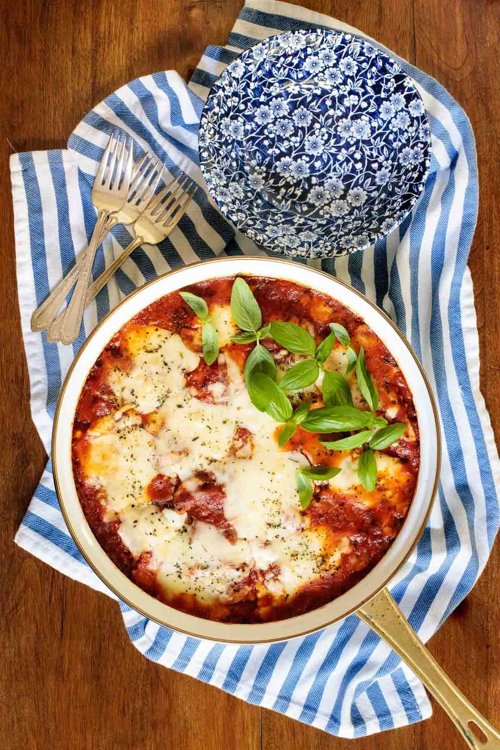 Chicken Sausage Lasagna in a white pot on a blue and white stripe towel.