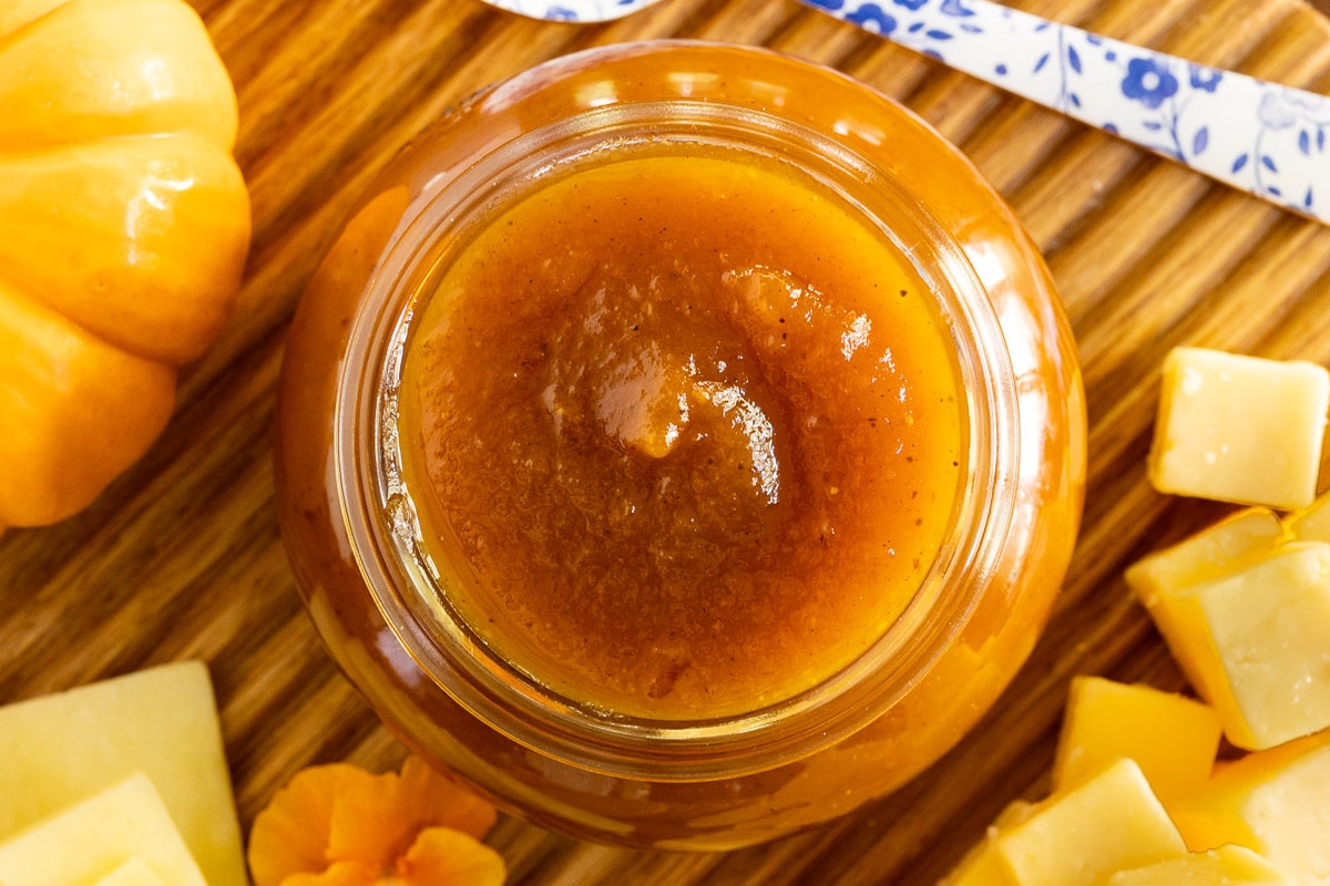 Horizontal overhead closeup photo of a jar of Pumpkin Jam (Confiture De Citrouille) on a fall appetizer tray.