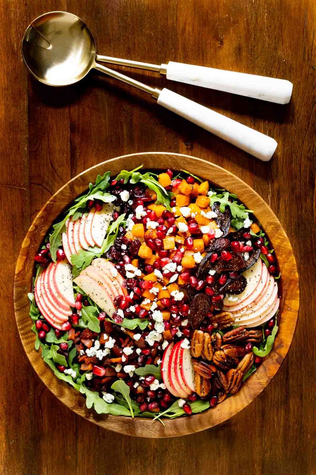 Vertical overhead photo of Harvest Apple Arugula Salad in a wooden serving bowl with serving utensils.