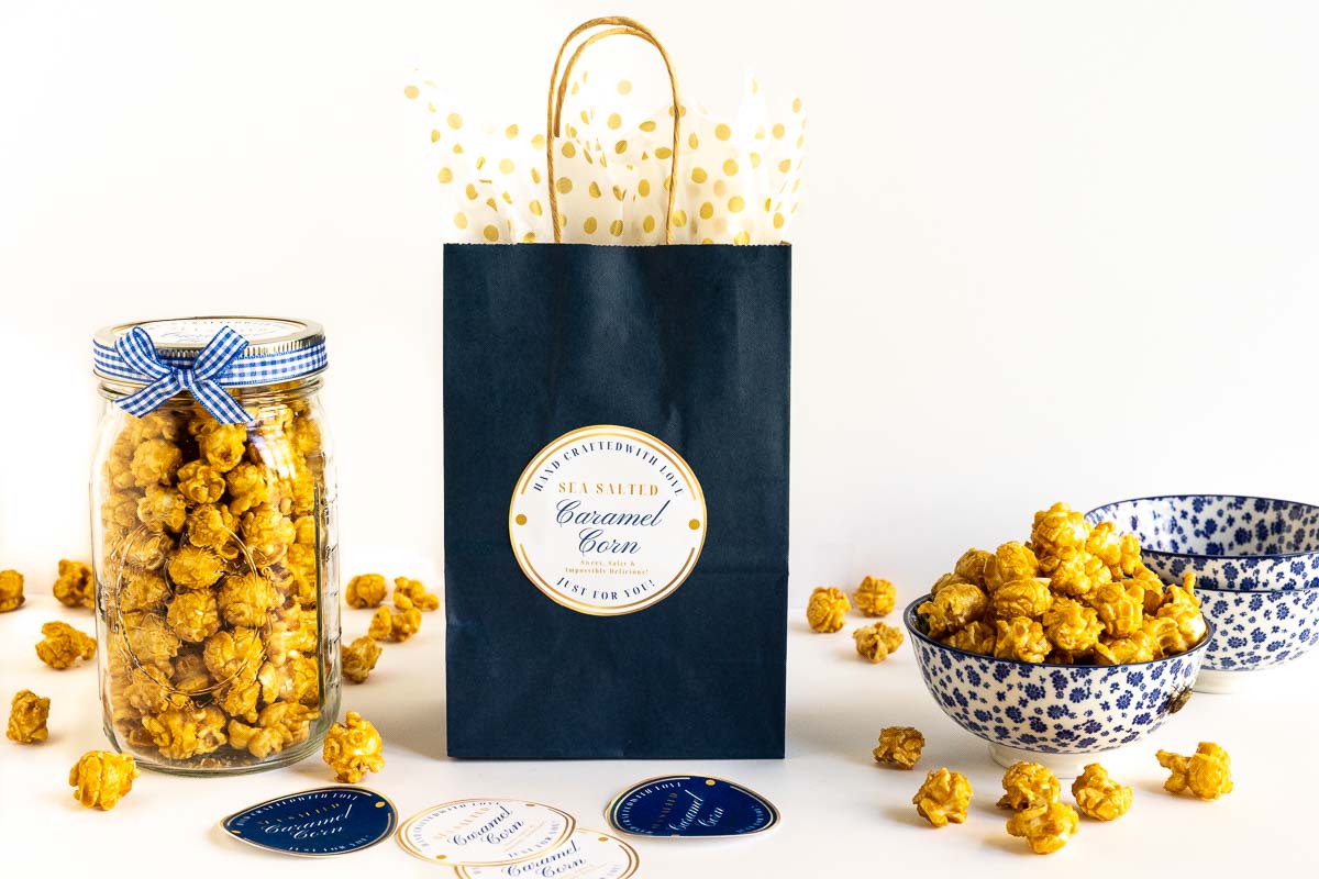 Horizontal photo of gift bags and Ball jars filled with Ridiculously Easy Sea Salted Microwave Caramel Corn with custom gift labels included.