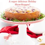 Vertical photo of a Ridiculously Easy Orange-Glazed Cranberry Cake on a white pedestal cake stand decorated with red and white checkered ribbon.