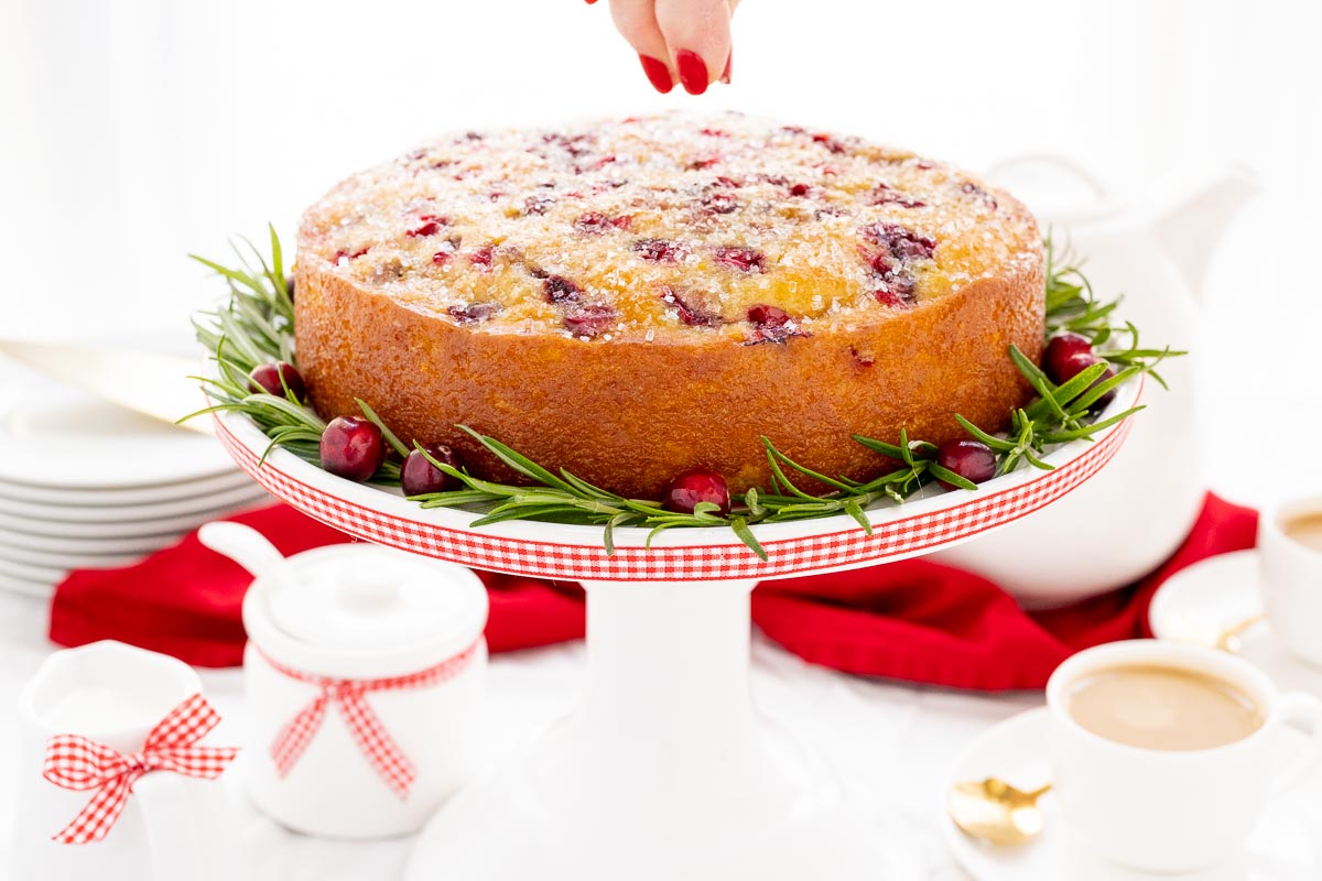 Horizontal photo of a Ridiculously Easy Orange-Glazed Cranberry Cake with sparkling sugar being sprinkled on top.