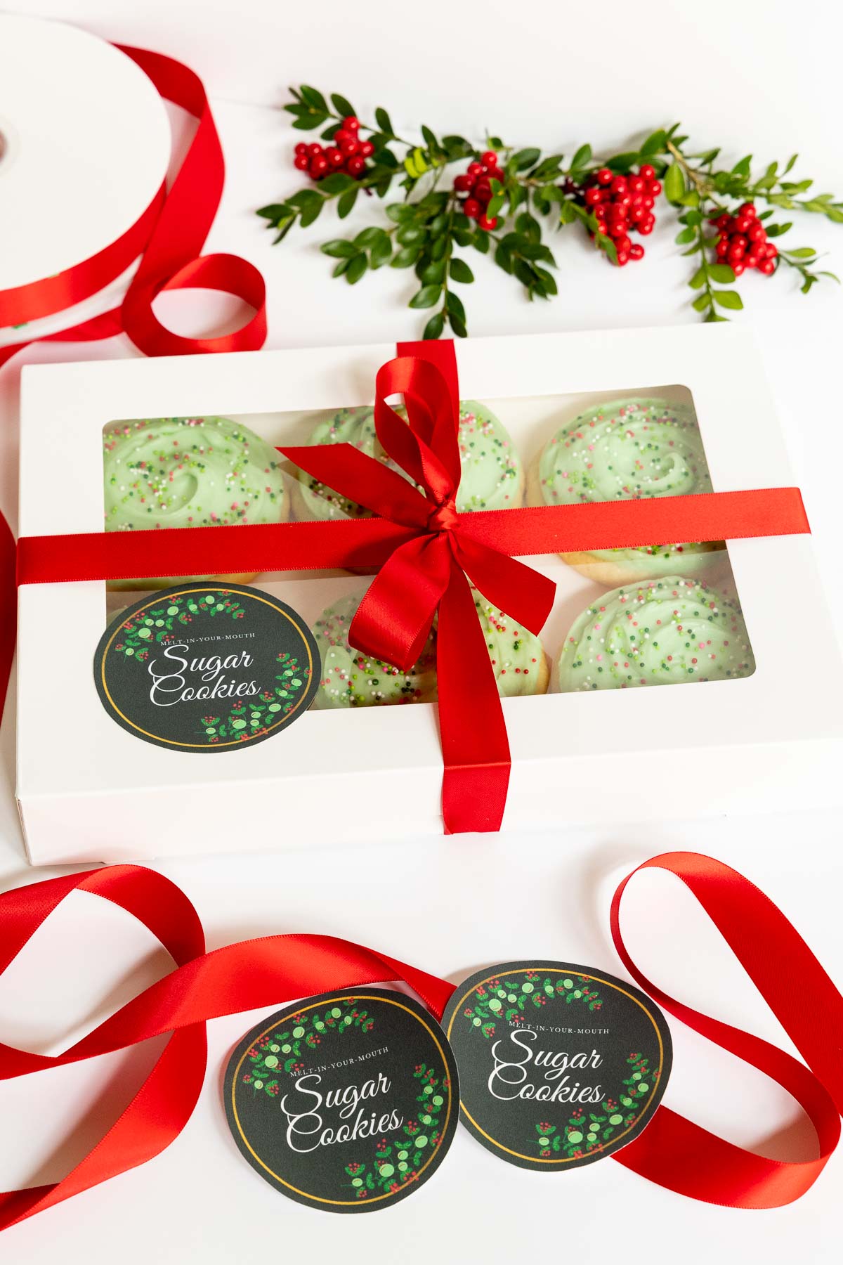 Vertical photo of Copycat Crumbl Christmas Sugar Cookies in gift boxes with red ribbon and custom gift labels.