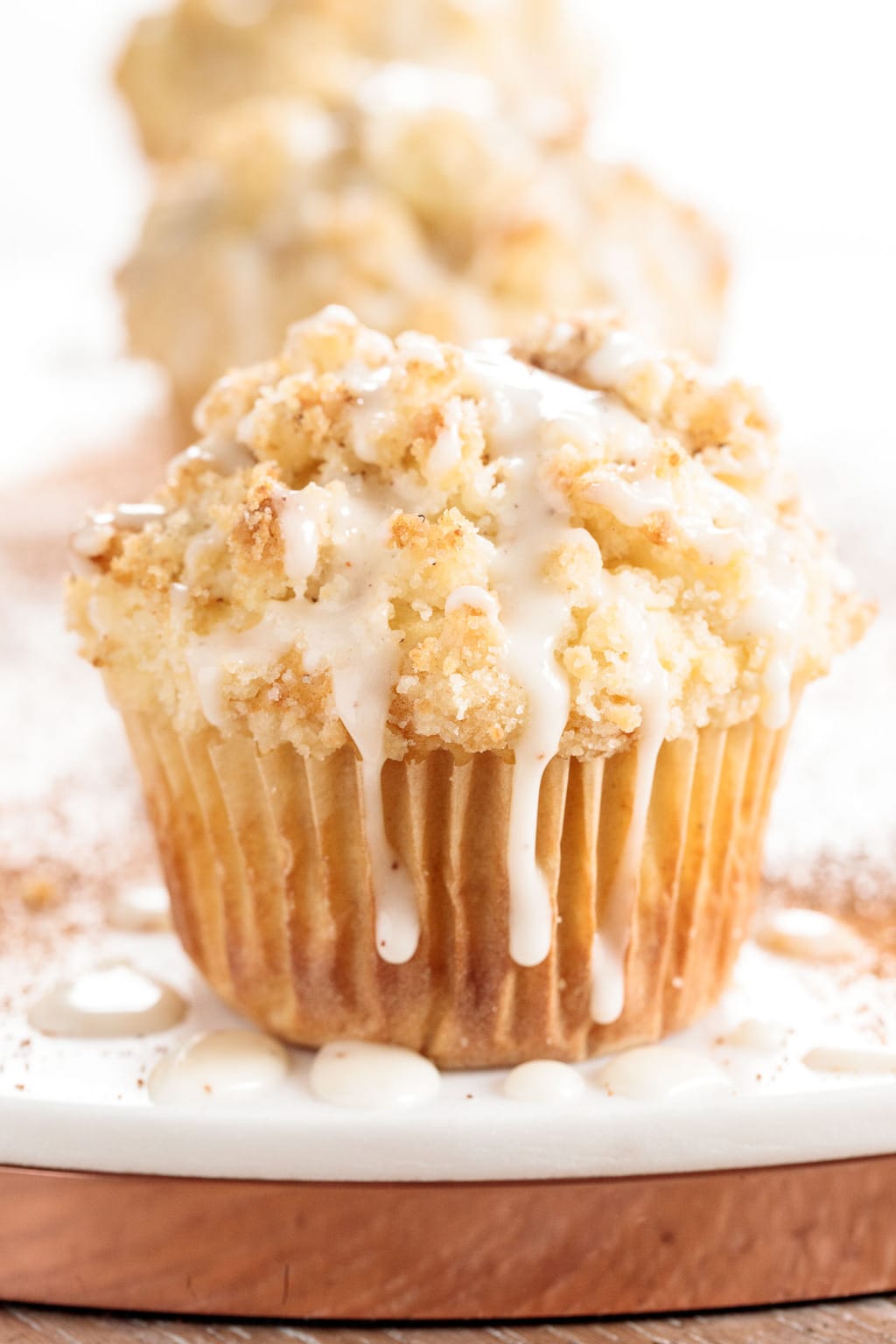 Vertical extreme closeup photo of a Eggnog Crumble Muffin on a white marble surface with icing drizzled down the sides.