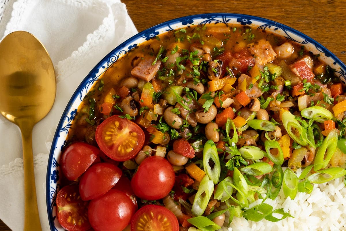 Horizontal overhead photo of a bowl of Healthy Hoppin' John with fresh sliced tomatoes, onions and white rice.