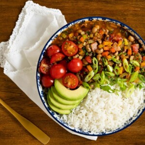 Horizontal overhead photo of a serving bowl of Healthy Hoppin' John with rice and sliced tomatoes, onions and avocados.