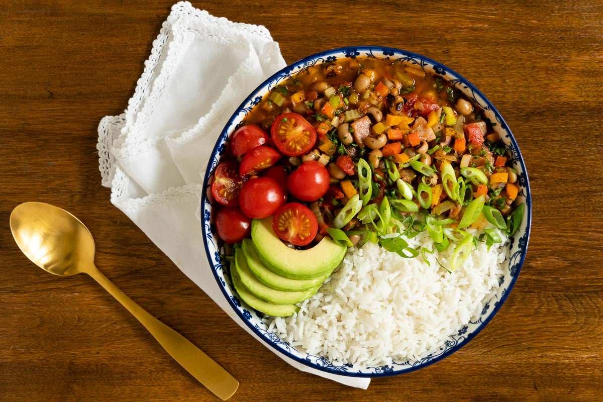 Horizontal overhead photo of a bowl of Healthy Hoppin' John with rice, sliced avocados, onions and tomatoes.