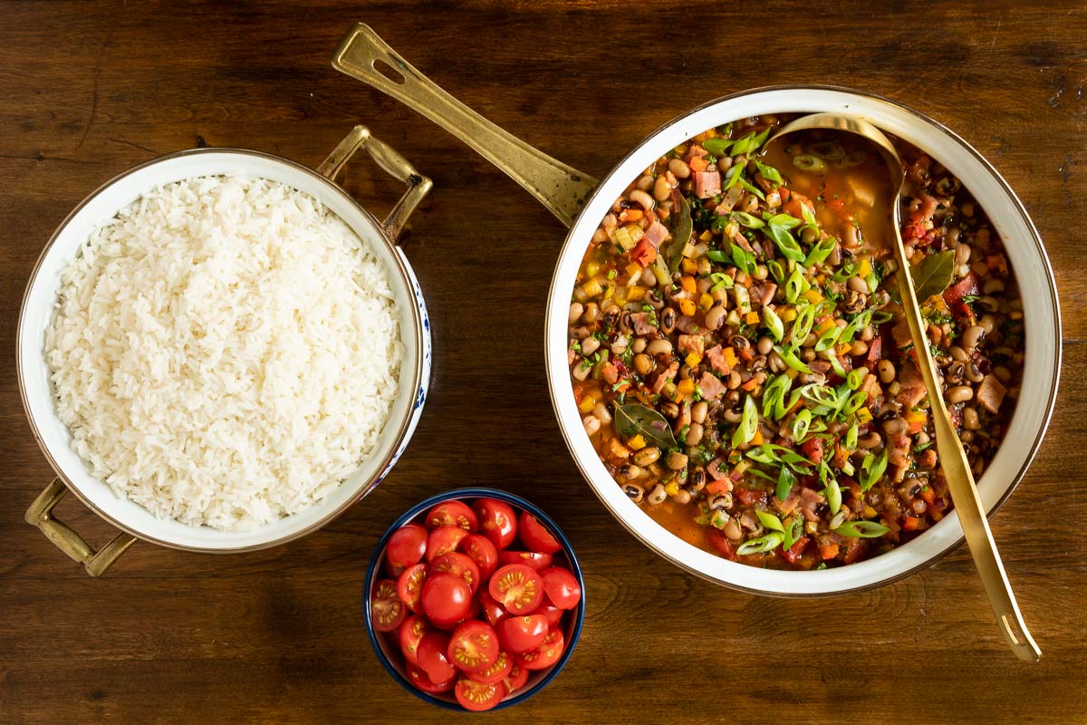 Horizontal overhead photo of a pan of Healthy Hoppin' John next to a pot of cooked white rice and a bowl of sliced tomatoes.