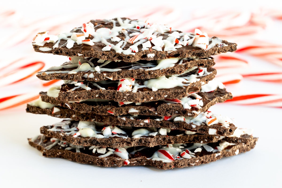 Horizontal closeup photo of a stack of Peppermint Bark Brittle with candy canes in the background.