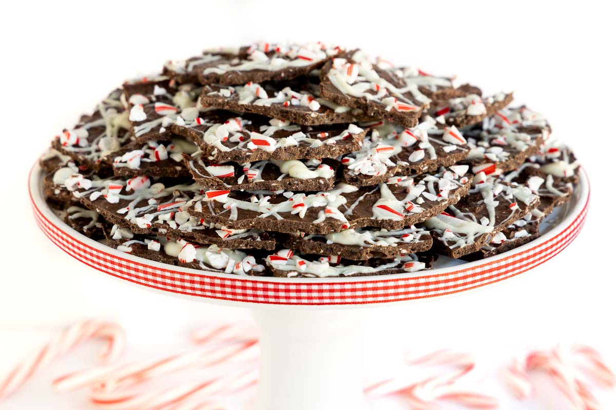 Closeup horizontal photo of a batch of Peppermint Bark Brittle on a white pedestal plate decorated with red and white checkered ribbon around the edge of the plate.