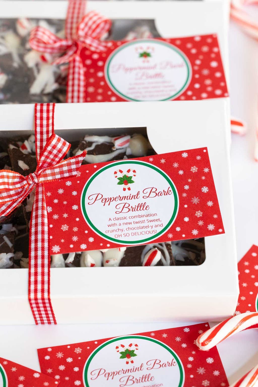 Vertical photo of Peppermint Bark Brittle in decorative white boxes with custom gifting labels attached.