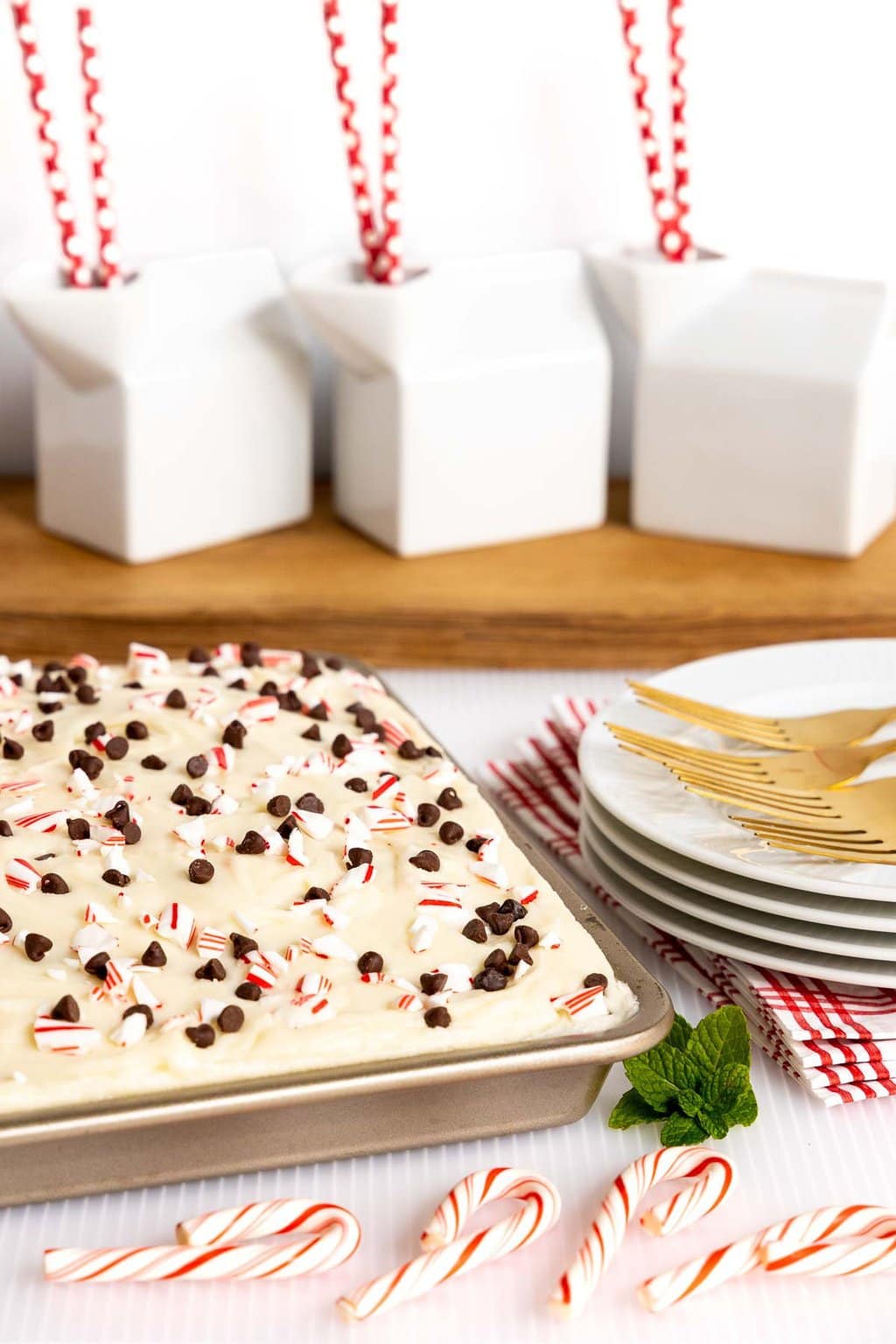 Vertical photo of a pan of Ridiculously Easy Chocolate Peppermint Sheet Cake with milk cartons in the background and candy canes in the foreground.