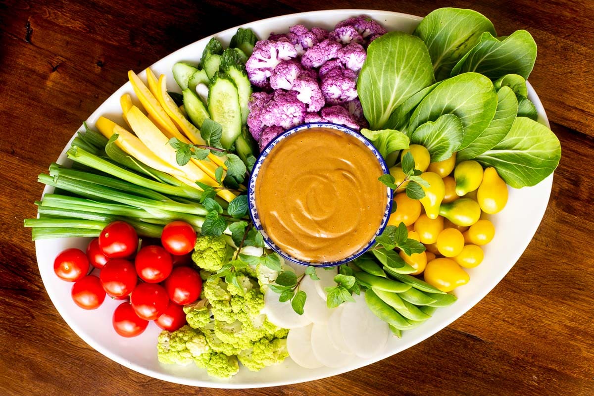 Overhead horizontal photo of an appetizer platter of vegetables featuring 5 Minute Easy Peanut Sauce in the center on a wood table.