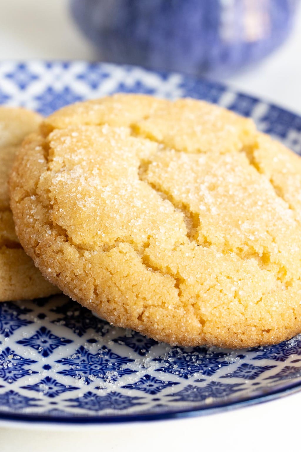 Vertical extreme closeup photo of a Crinkly Crackly Lemon Sugar Cookie on a blue and white patterned plate.