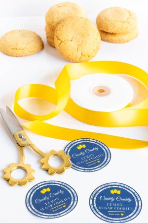 a pile of lemon cookies with a swirl of bright yellow ribbon, decorative scissors and 3 custom made labels perfect for gifting