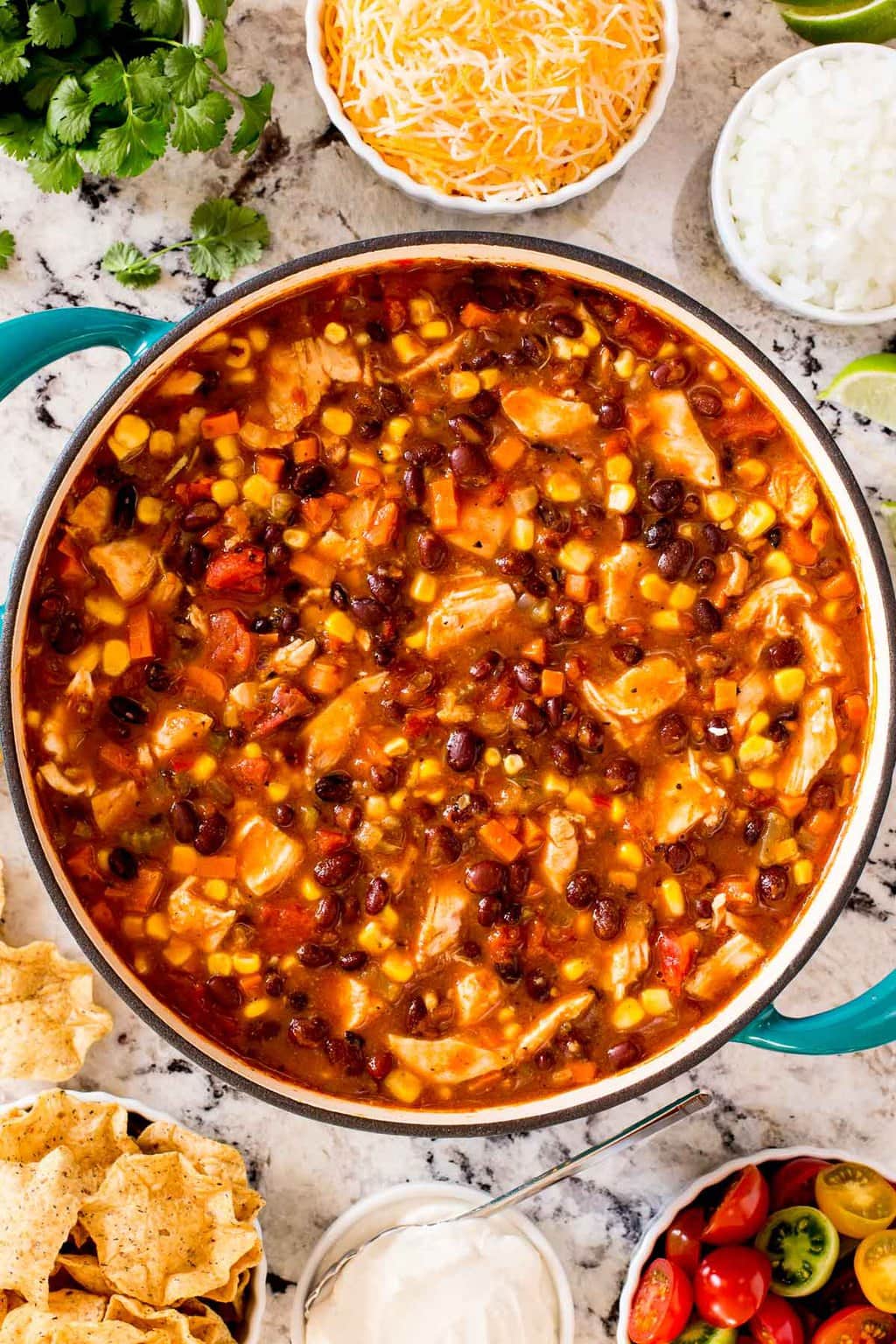 Overhead vertical photo of a pot of Healthy Chicken Black Bean Chili surrounded by garnishes and tortilla chips.