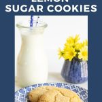 Vertical photo of two Lemon Sugar Cookies on a blue and white patterned plate with a jar of milk and a vase of yellow flowers in the background.