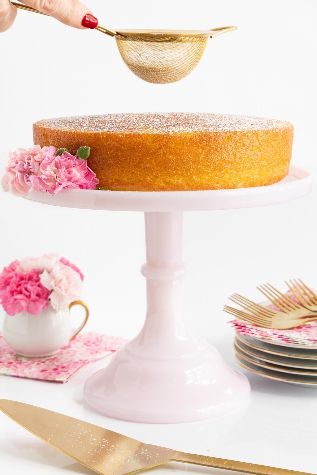 Vertical closeup photo of Ridiculously Easy French Butter Cake on a pale pink pedestal cake stand decorated with flowers.