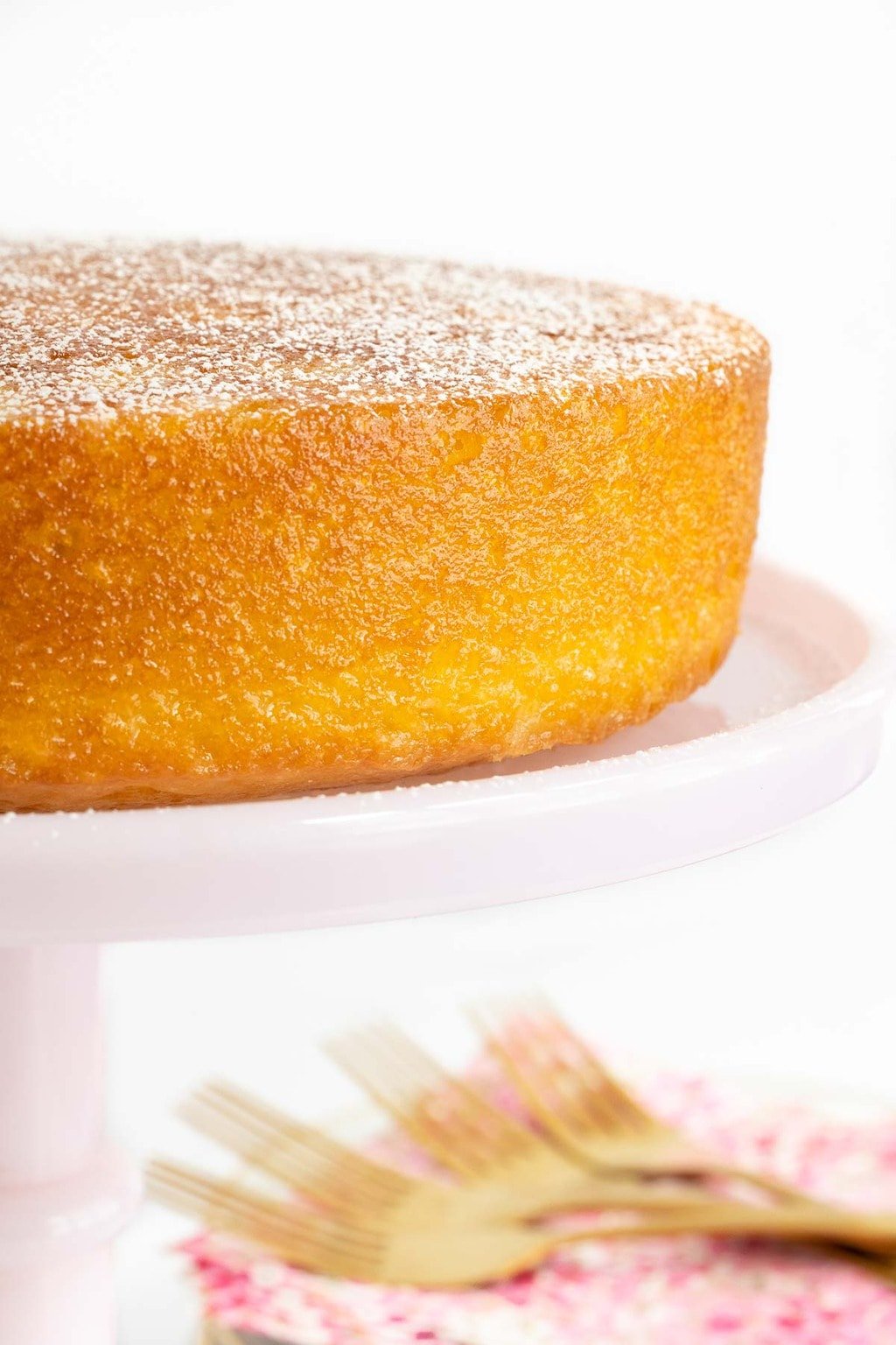 Vertical closeup photo of a Ridiculously Easy French Butter Cake with powdered sugar on top sitting on a pink glass pedestal cake stand.
