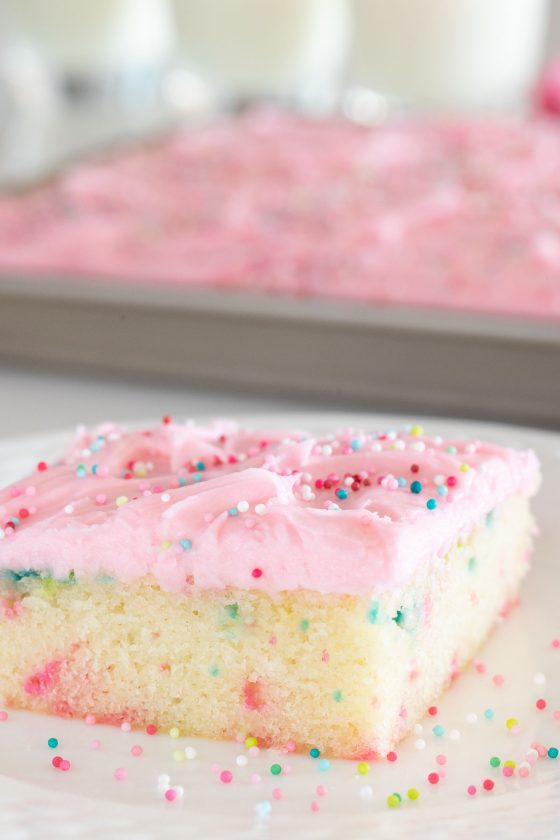 Vertical closeup photo of a Ridiculously Easy Funfetti Sheet Cake on a white serving plate covered in colorful sprinkles.