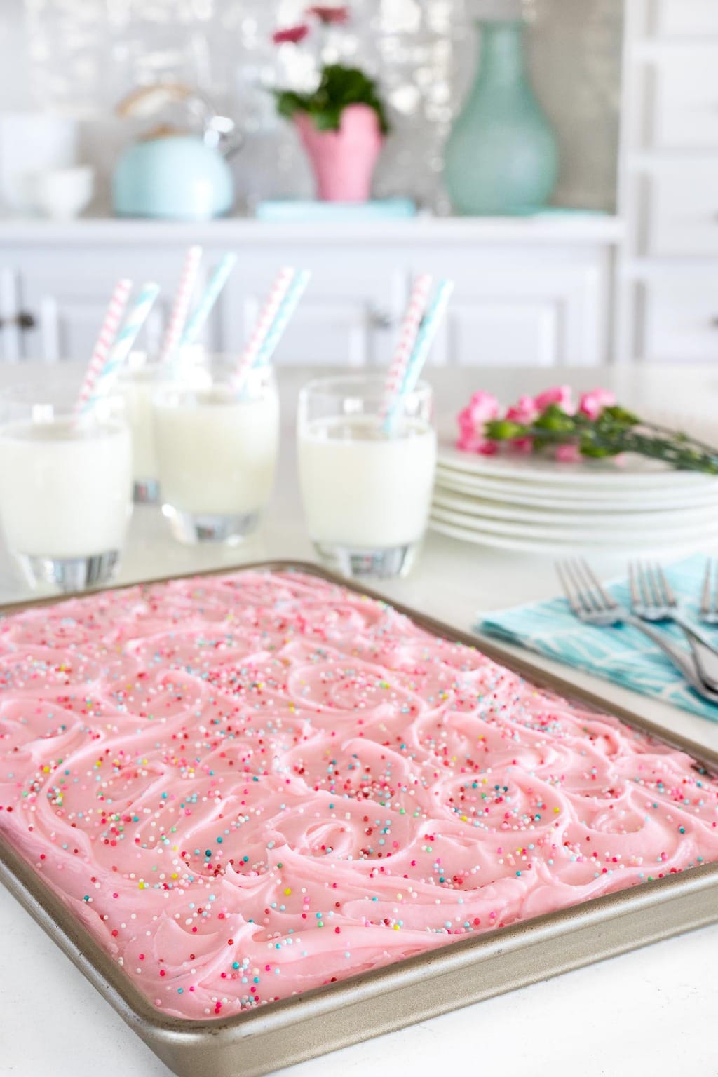 Vertical closeup photo of a Ridiculously Easy Funfetti Sheet Cake on a white kitchen island with glasses of milk in the background.