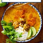 Vertical overhead photo of a dish of Thai Coconut Soup with Chicken Cilantro Meatballs garnished with fresh herbs on a wood table.
