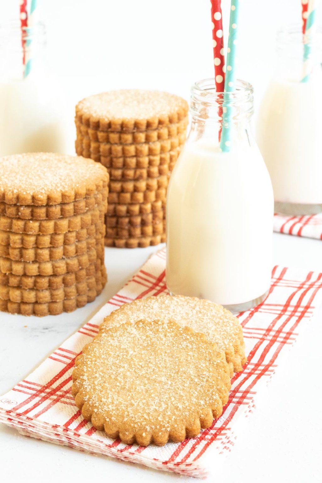 Vertical photo of Mexican Cinnamon Sugar Shortbread Cookies in stacks with glasses of milk in the background.