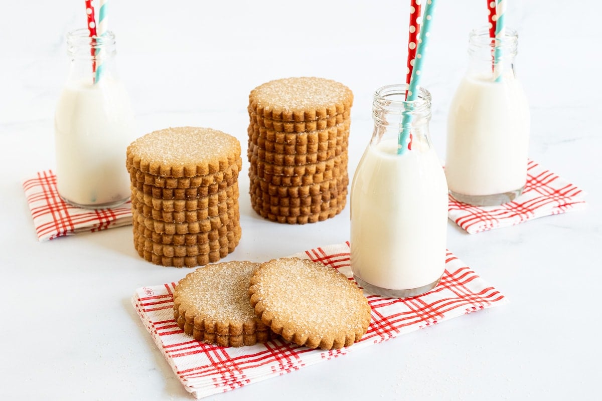 Horizontal photo of a batch of Mexican Cinnamon Sugar Shortbread on red and white patterned napkins with small bottles of milk with straws.