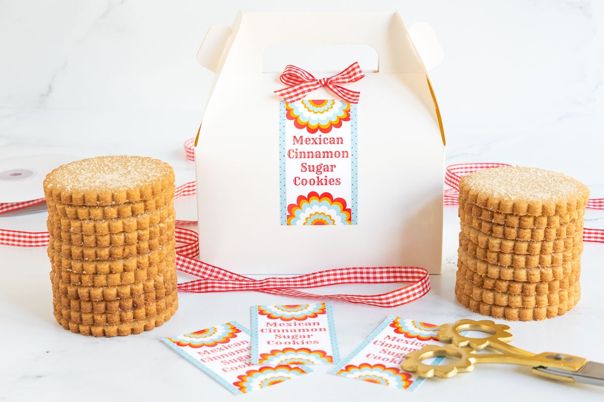 Horizontal photo of stacks of Mexican Cinnamon Sugar Shortbread around a decorative gift box with custom gift-giving labels.