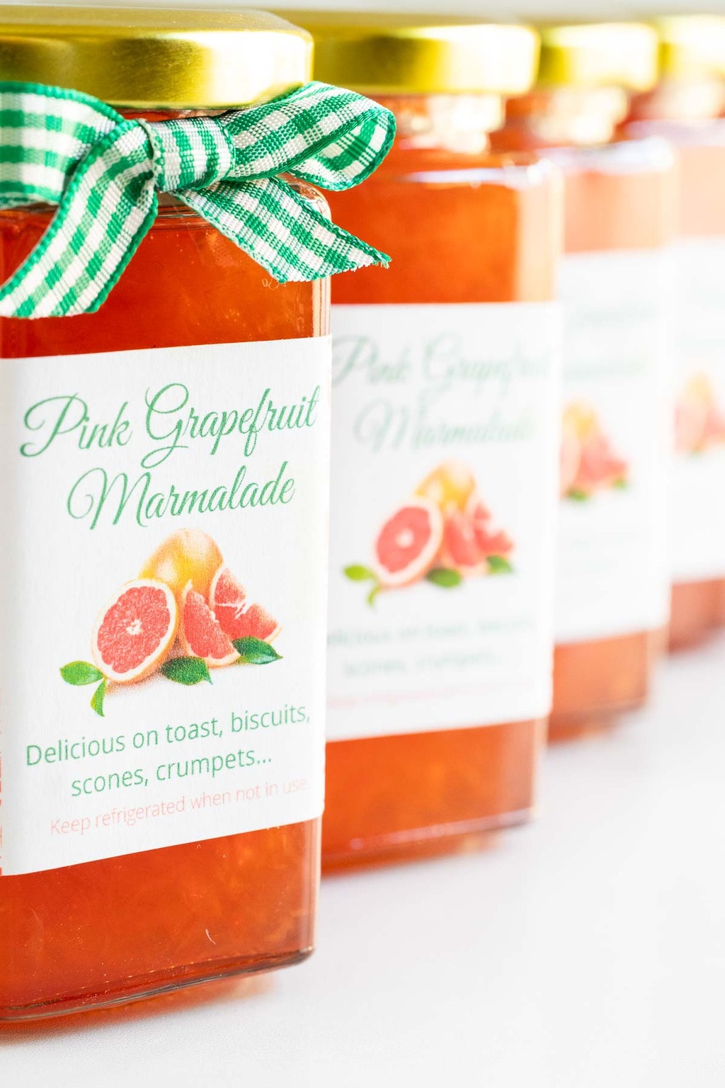 Vertical extreme closeup photo of a row of jars of Pink Grapefruit Marmalade with custom labels and decorative ribbons.