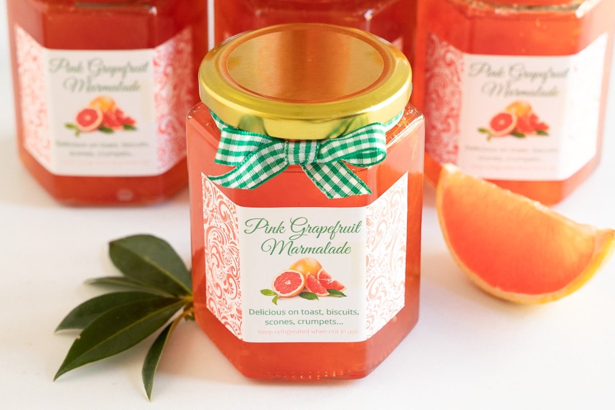 Horizontal closeup photo of jars of Pink Grapefruit Marmalade with custom gift labels and green and white checkered ribbon.