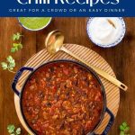 Vertical overhead photo of a cast iron pot of Black Bean Turkey Chili surrounded by fresh garnishes with a title graphic at the top of the photo.