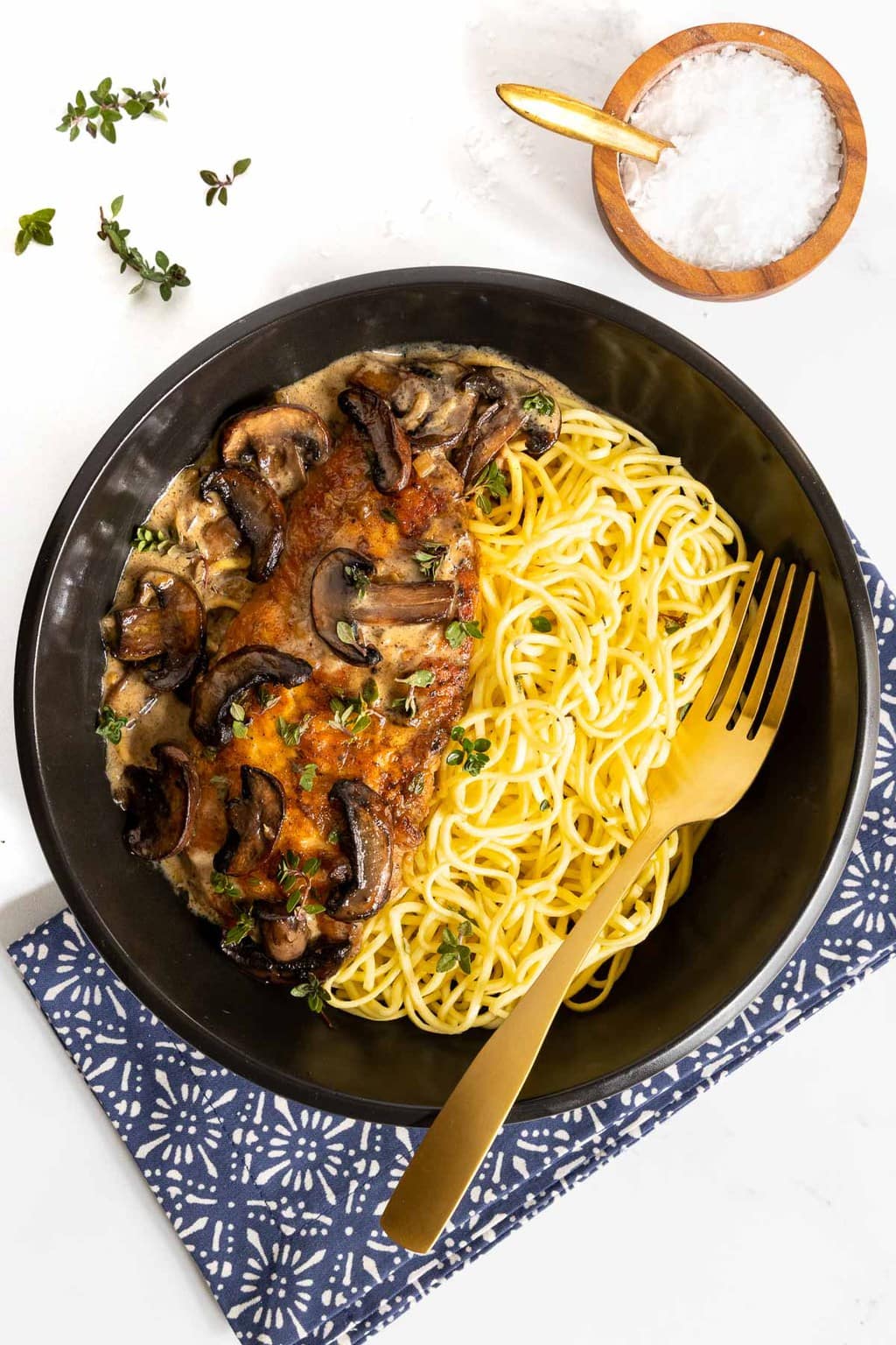 Vertical overhead photo of Weeknight or Dinner Party Chicken Marsala in a black serving bowl with a side of pasta.
