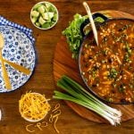 Horizontal overhead photo of a pot of Southwestern Black Bean Chicken Tortilla Soup surrounded by garnishes and tortilla strips.
