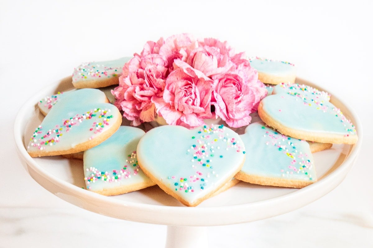 Horizontal photo of a batch of pale turquoise Valentine Shortbread Cookies on a white pedestal serving plate.