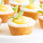 Horizontal closeup photo of a batch of Ridiculously Easy Lemon Curd Shortbread Tarts garnished with fresh mint leaves.